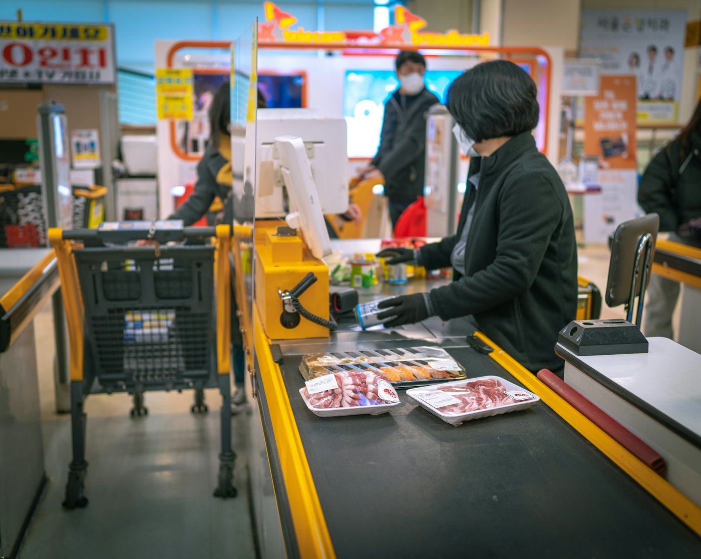 A person paying at a supermarket checkout with a loaded cart.