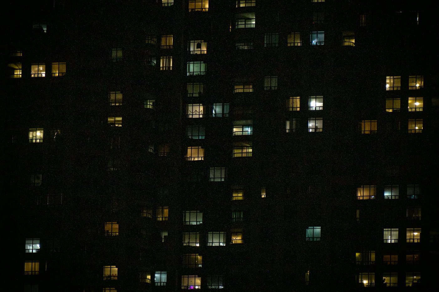 A dark apartment block at night with scattered lit windows.