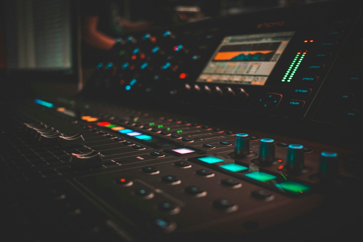 A close-up of a lit audio mixing desk with faders and knobs.
