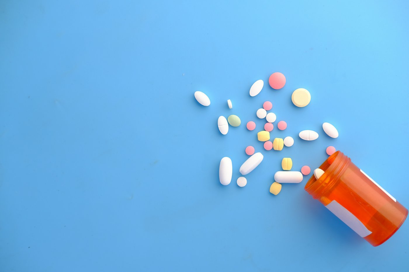 Colourful pills spilling from an orange prescription bottle.