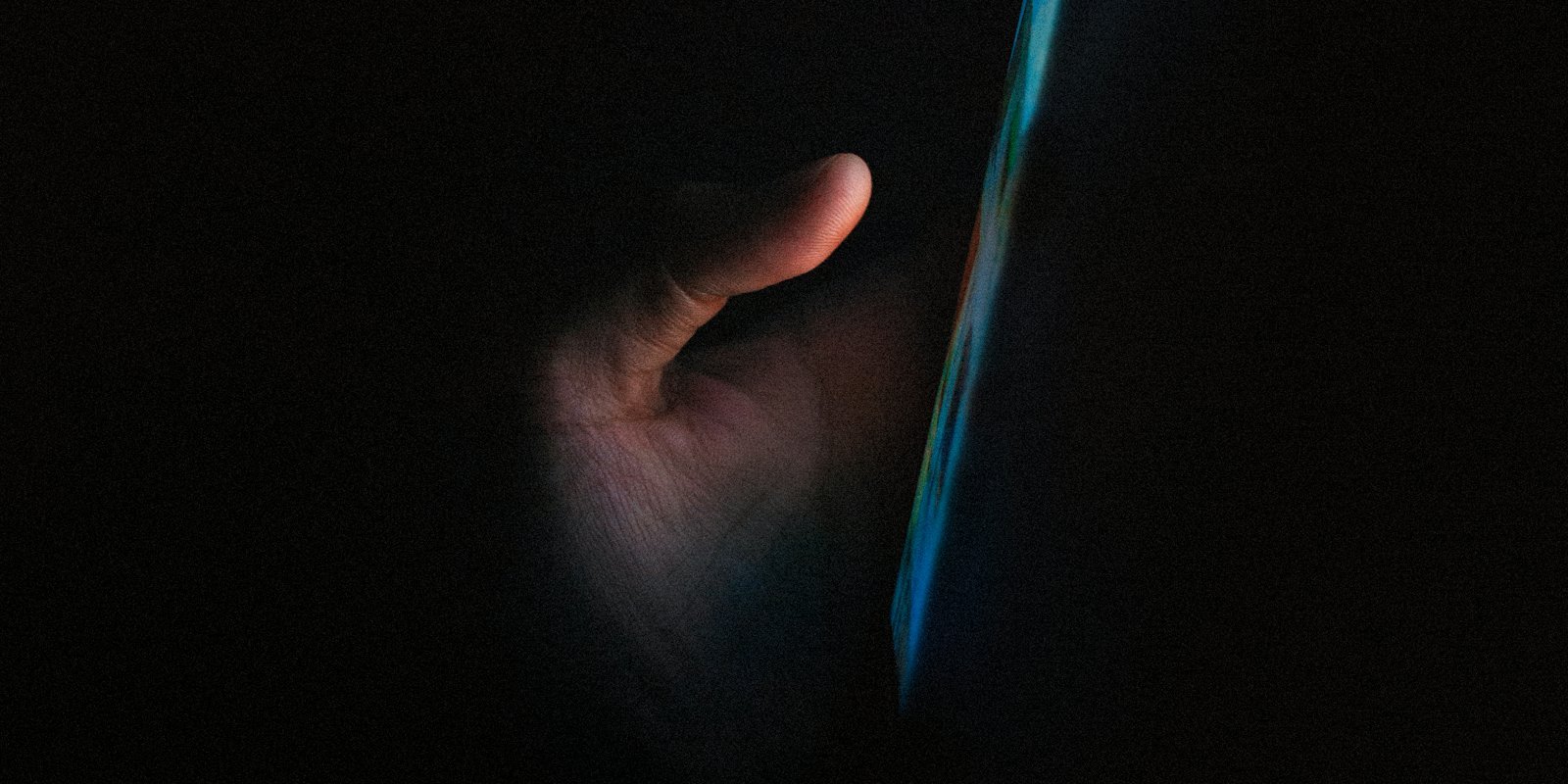 A hand lit only by the glow of a phone screen in a dark room.